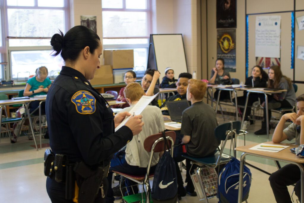 A female police officer in uniform teaches a lesson to students in a classroom